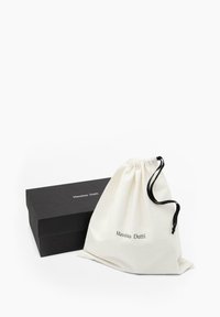 Bawełniany worek ze sznurkiem w kremowym kolorze z czarnym sznurkiem, oznaczony napisem "Massimo Dutti", obok czarnego pudełka tekturowego z tym samym logo.