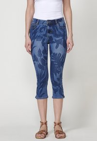 Pantalons capri en denim avec un motif floral bleu, taille mi-haute et cinq poches. Fini avec un ourlet roulé et une couture contrastante.