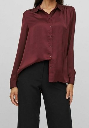 Donker bordeaux zijden blouse met een puntige kraag, lange mouwen en een knoopsluiting aan de voorkant, gecombineerd met zwarte wijde broek.