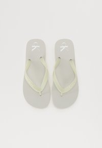 Grå flip-flops med lysegrønne stropper, med en hvit logo og merkevarenavn trykt på sålen. Jevn tekstur, minimalistisk design.