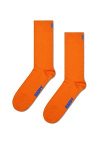 Pomarańczowe skarpetki bawełniane o gładkiej teksturze, z niebieskim napisem "HAPPY" w pobliżu kostki oraz długością do połowy łydki.