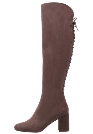 Brun ruskind knæhøj støvle med blokhæl og snøredetalje, der løber lodret langs bagsiden.