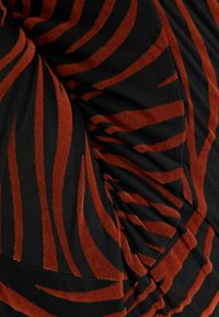 Czarna tkanina z wystającymi, rustykalno-pomarańczowymi paskami z aksamitu, skręconymi w celu uzyskania fałd i tekstury.