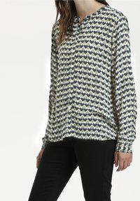 Camicia con bottoni caratterizzata da un motivo geometrico a zigzag in verde, blu navy e bianco. Maniche lunghe con orlo dritto e texture morbida.