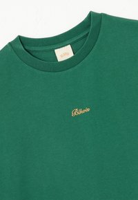 Grønn bomull T-skjorte med rund hals, korte ermer og en liten gullbrodert logo på brystet. Glatt tekstur, uformell design.