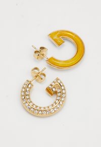 Boucles d'oreilles en ton or présentant un design courbé. L'une a un incrustation en résine jaune ; l'autre a des strass clairs disposés en motif spirale.