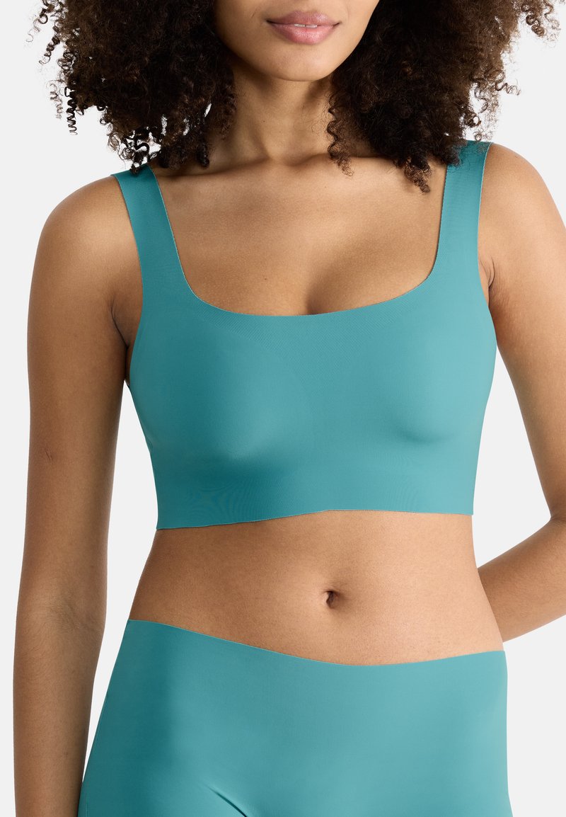 Turkise sømløs BH med brede stropper, firkantet udskæring og glat tekstur. Stoffet er strækbart, uigennemsigtigt, med ingen synlige lukninger.