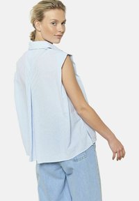 Camicetta senza maniche a righe blu e bianche, con vestibilità rilassata, dettaglio piega sul retro e morbido tessuto di cotone. Abbinata a jeans in denim blu chiaro.