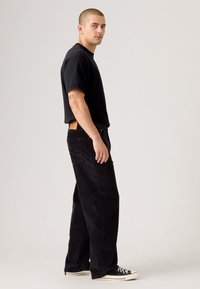 Black cotton t-shirt with a crew neckline, paired with wide-leg black corduroy pants and black sneakers with white soles and laces.