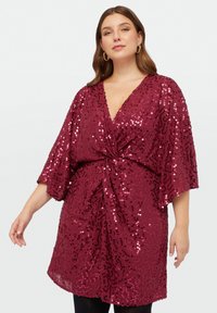 Robe en sequins bordeaux avec un décolleté en V, des manches kimono courtes et un devant torsadé. Elle présente une texture douce et une coupe décontractée.