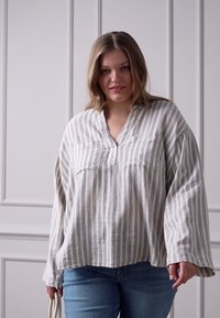 Blusa leve e riscada com decote em V e mangas longas e largas; feita de tecido macio em tons neutros; apresenta um bolso na frente.