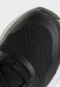 Scarpa da ginnastica nera con tomaia in mesh testurizzato, dettagli in pelle liscia e suola in gomma bianca. Inclusi lacci e occhielli robusti.