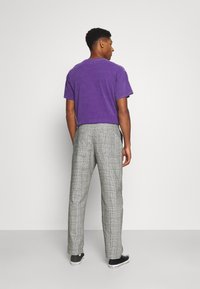 Purple cotton t-shirt and gray plaid trousers. T-shirt is short-sleeved with a relaxed fit; trousers have a straight leg and side pockets.