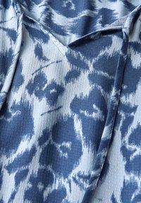 Tessuto blu e bianco con un motivo a superficie testurizzata e un leggero lucido. Il design presenta forme astratte e uno stile chambray.
