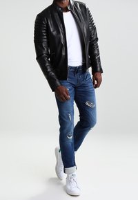 Svart läderjacka med ribbade axeldetaljer, vit t-shirt, slitna blå jeans och vita sneakers med gröna detaljer.