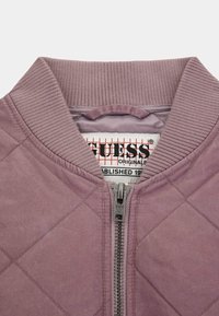Quilted bomber jacket in light purple with ribbed collar. Features a silver zipper and branded label inside. Smooth texture.