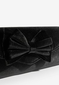 Czarna kopertówka z teksturowanej tkaniny, z dużą kokardą z przodu, subtelnie błyszczącą.