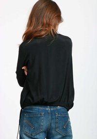 Blusa nera a maniche lunghe con una vestibilità ampia e vita arricciata, abbinata a jeans in denim blu con dettagli di cucitura discreti sulle tasche.