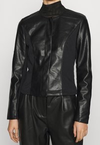 Czarna skórzana i materiałowa kurtka z wysokim kołnierzem, o dopasowanym kroju i kontrastowych panelach, gładkiej fakturze oraz zapięciu na zamek.
