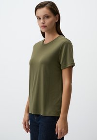 T-shirt verde oliva a maniche corte, scollo rotondo, tessuto morbido, vestibilità comoda, abbinato a jeans blu scuro. Design minimalista senza motivi.