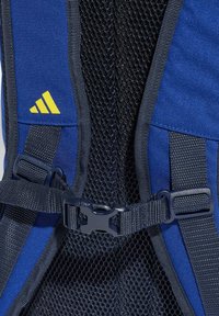 Mochila azul con respaldo de malla, correas ajustables y un broche negro. Acentuada con un logo amarillo. Tejido texturizado con costuras reforzadas.