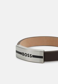 Brun läderbälte med en metallspänne med borstad finish, graverad med "BOSS" och accentuerad med ett svart streck.