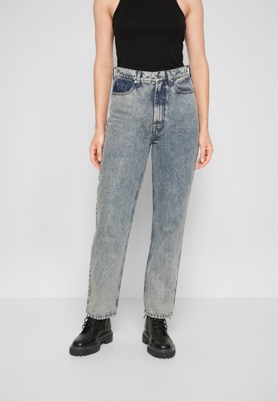 Jeans de ganga de cintura alta, lavagem clara, com corte reto, apresentando um leve desbotado e um design clássico de cinco bolsos, combinados com botas pretas.