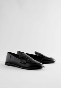 Mustad nahast loafers sileda tekstuuriga, dekoratiivse rihma ja õmblemise detailidega ning madala, tasase tallaga.