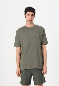 Olivgrünes T-Shirt mit kurzen Ärmeln aus weichem Stoff. Hat einen runden Ausschnitt und ein kleines Logo auf der Brust. Kombiniert mit passenden Shorts.
