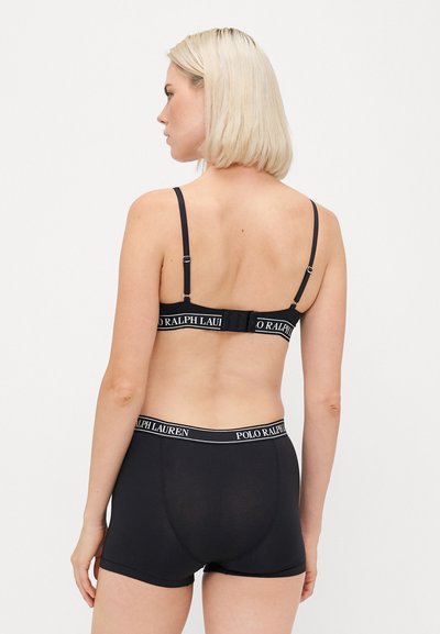 Čierna podprsenka a zodpovedajúce nohavičky v štýle boyshorts vyrobené z hladkej látky, s elastickým pásom so značkou. Jednoduchý dizajn s nastaviteľnými ramienkami.