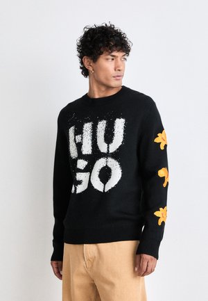 Maglione a maglia nera con grande grafica bianca "HUGO", ricamo floreale giallo sulle maniche, scollatura a girocollo e polsini e bordi a coste.