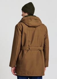 Cappotto marrone con cappuccio e vita cinturata, caratterizzato da una texture liscia e una finitura leggermente lucida. Abbinato a un berretto di maglia verde.