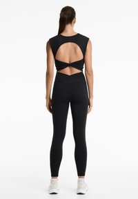 Completo sportivo nero con top senza maniche e apertura circolare nella parte posteriore, abbinato a leggings a vita alta. Materiale liscio e elastico.