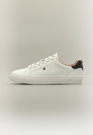 Valkoinen matala tennari, jossa valkoiset nauhat, sivussa pieni kultainen "W" ja musta kantapään nauha hienovaraisella tekstuurilla sekä beige vuori.