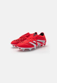 Red soccer cleats with mesh-knit upper, textured accents, silver detailing, and multiple transparent studs on the sole for traction.