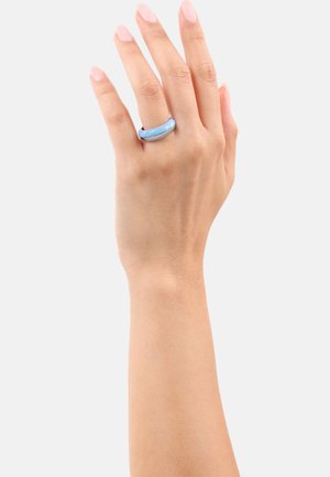 Hand met een lichte huidskleur die een gladde, glanzende, lichtblauwe en zilveren ring om de middelvinger draagt, tegen een eenvoudige witte achtergrond.