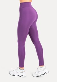 Paarse leggings met hoge taille, gemaakt van rekbare stof, met een gladde textuur en een aansluitend ontwerp. Gedragen met witte sneakers.