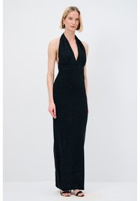 Schwarzes Halter-Kleid mit tiefem V-Ausschnitt, verziert mit weißen Punkten. Dünne Träger und eine figurbetonte Silhouette, die bis zum Boden reicht.