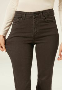Jean taille haute marron foncé avec cinq poches, passants de ceinture et fermeture à bouton, mettant en valeur une texture en denim lisse et une coupe cintrée.