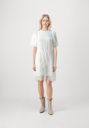 Weißes Spitzenkleid mit Puffärmeln und gewelltem Saum. Aus strukturiertem Stoff gefertigt, mit kunstvollen floralen Mustern. Tragen mit beigen Cowgirl-Stiefeln.