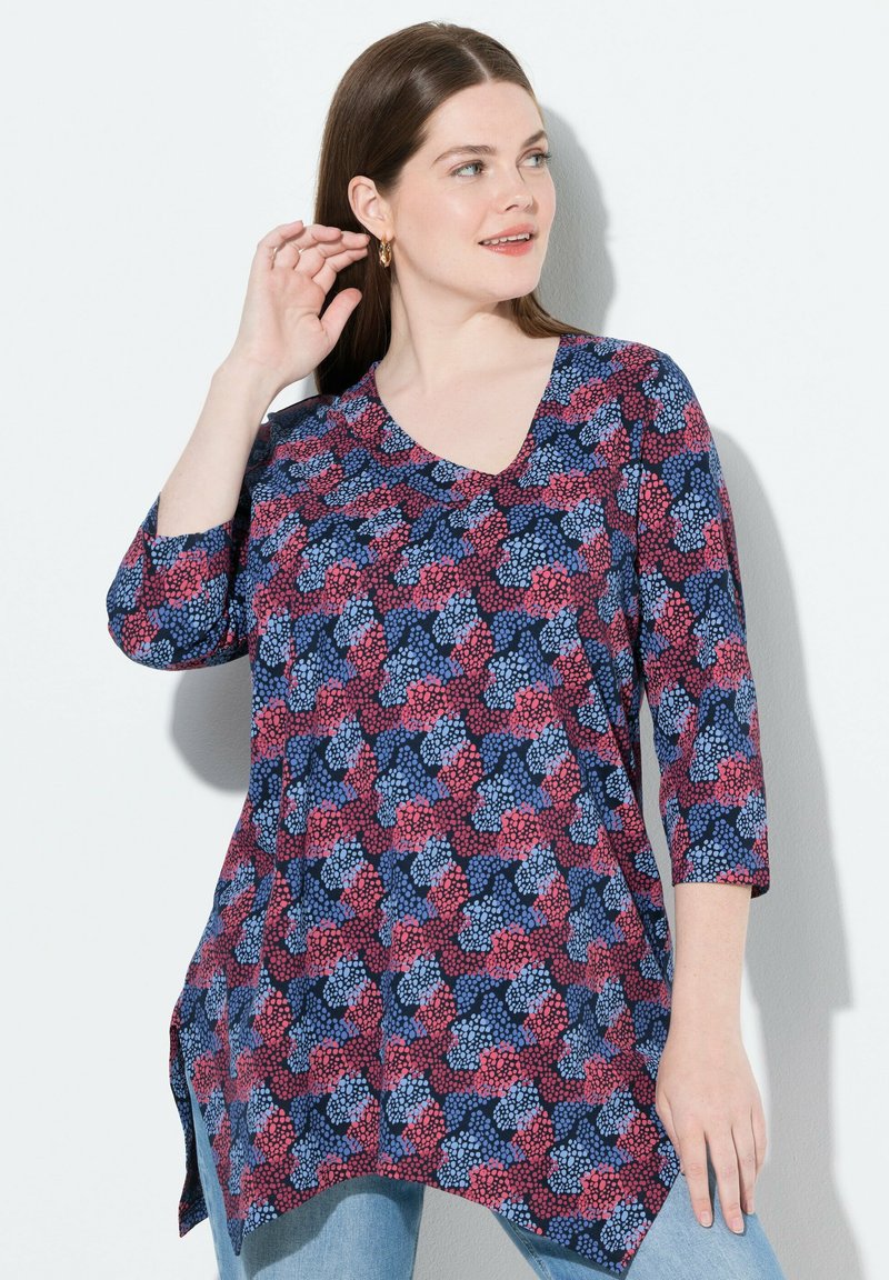 Blaue, rote und rosa gemusterte Tunika mit V-Ausschnitt, 3/4-Ärmeln und seitlichen Schlitzen. Hergestellt aus weichem Stoff mit leichter Textur.