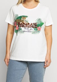Vit bomull t-shirt med en tiger grafik, gröna blad och färgglada blommiga detaljer. Texten lyder "Paradaze Wish you were here!"