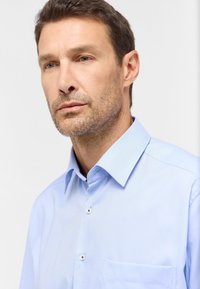 Hellblaues, knöpfbares Hemd mit spitzem Kragen, glatter Textur, einer Brusttasche und dezentem diagonalen Muster.