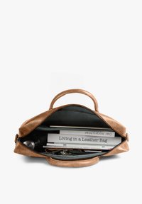 Brown leather bag open to show a laptop, books including "Living in a Leather Bag," papers, and a set of keys inside.