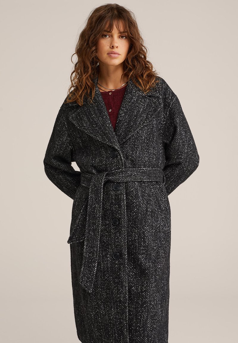 Črno-bele plašč z vzorcem ribje kosti, z pasom, velikim ovratnikom in gumbom za zapiranje. Teksturojeno volneno blago. Dolgi rokavi.