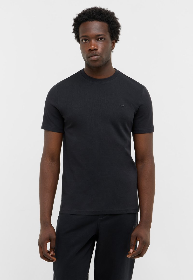 T-shirt noir à manches courtes en tissu lisse et extensible. Doté d'un col rond et d'un petit logo sur la poitrine. Design simple et ajusté.