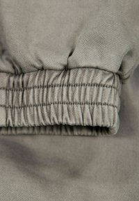 Helle graue Stoffmanschette mit Raffungen und gerippter Textur. Glatte Oberfläche mit sichtbaren Nähdetails entlang des Randes.