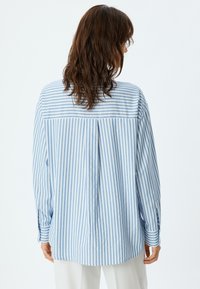 Lichtblauw en wit gestreept shirt van zachte stof, met een losse snit, lange mouwen en een ronde zoom met knoopmanchetten.