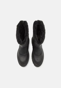 Botas negras impermeables con un exterior de cuero suave, un forro de piel de oveja negra en el cuello y una suela de goma texturizada.