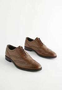 Pantofi de dress din piele maro, cu detalii brogue, vârf ascuțit și talpă neagră. Prezintă șireturi și perforații decorative pe margini.